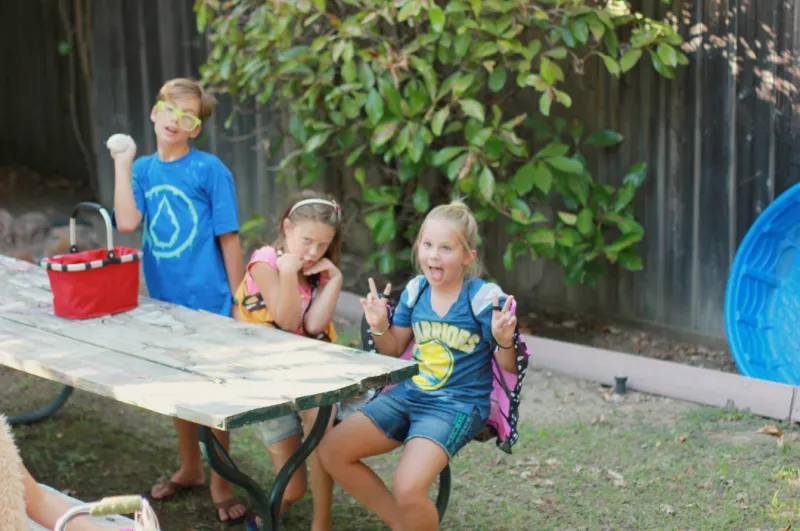 Three kids are sitting in the backyard and posing for the camera