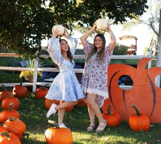 Family wearing coordinated fall-toned outfits walking together through a pumpkin patch